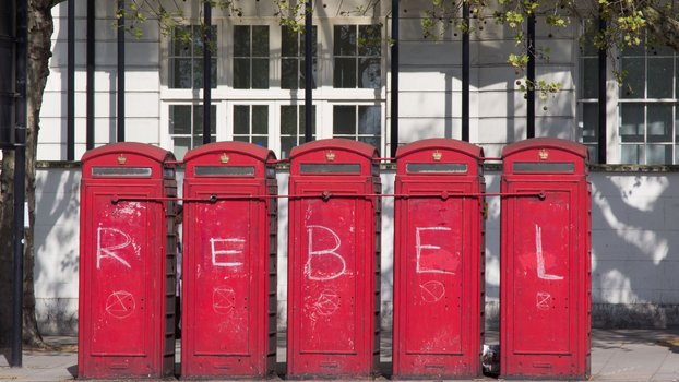 Fünf britische rote Standbriefkästen, darauf Graffiti: REBEL und Zeichen für Extinction Rebellion