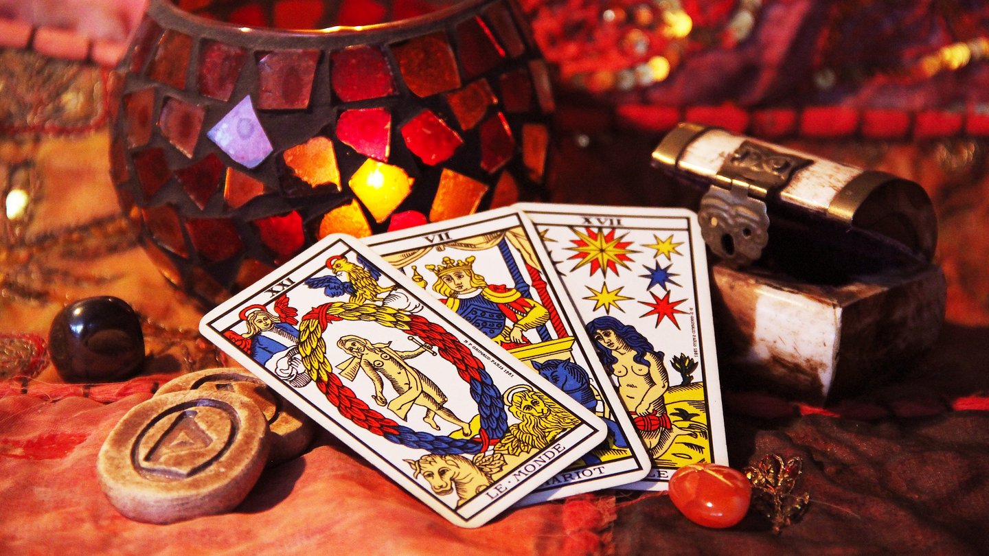 Komposition von verschiedenen Gegenständen auf einem Tisch, die für das Wahrsagen verwendet werden - u. a. drei Tarot-Karten.
