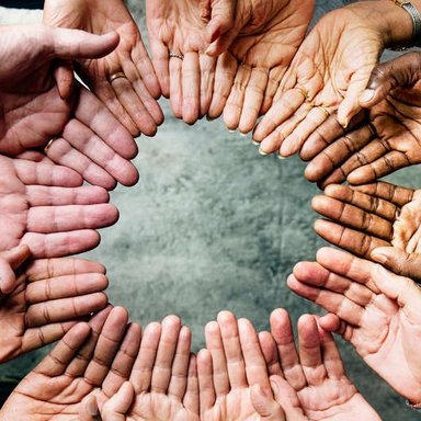 Nahaufnahmen von Händen einer multikulturellen Gruppe Menschen, die einen Kreis bilden.
