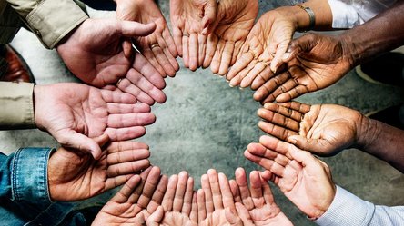 Nahaufnahmen von Händen einer multikulturellen Gruppe Menschen, die einen Kreis bilden.