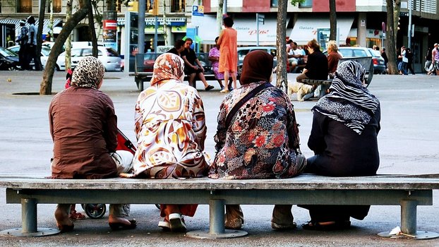 Rückansicht von vier kopftuchtragenden Frauen in langen Kleidern auf einer Bank sitzend