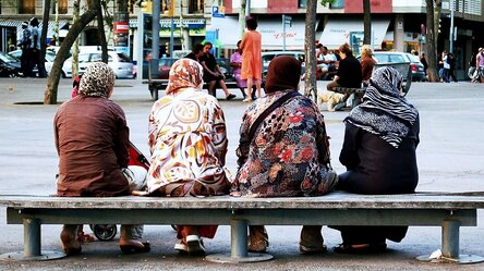 Rückansicht von vier kopftuchtragenden Frauen in langen Kleidern auf einer Bank sitzend