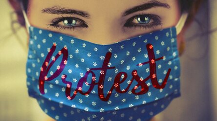 Eine Frau trägt eine Maske (Corona) mit der Aufschrift Protest